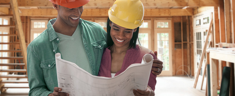 A couple with construction hats on, looking at a blueprint together