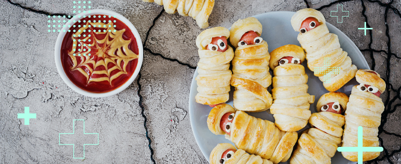 Hot dogs decorated as mummies with a bowl of ketchup 