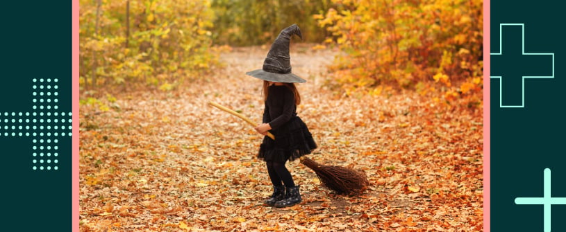 A child in a witch's costume riding a broom in the woods