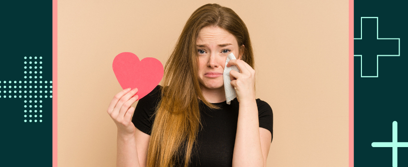 Woman whipping tear with tissue, while holding a paper heart.